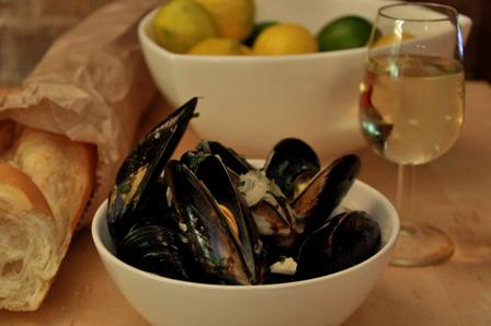 An image of moules mariniere, bread and wine with lemons in a bowl